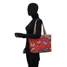 Load image into Gallery viewer, Mannequin in black attire with a Fabric with Leather Trim Zip Top City Tote - 12005 from Anuschka featuring a leather shoulder strap.
