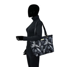 Load image into Gallery viewer, A person in a black bodysuit and full-head mask holding an Anuschka Fabric with Leather Trim Zip Top City Tote - 12005 handbag with a leather shoulder strap.
