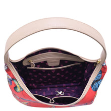 Load image into Gallery viewer, An open, patterned Anuschka handbag with a cream-colored shoulder strap and a purple interior displaying zippered pockets and brand logo.
