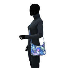 Load image into Gallery viewer, Mannequin dressed in a black bodysuit and gloves carrying a colorful floral Anuschka Fabric with Leather Trim East/West Hobo - 12013 with an adjustable handle.
