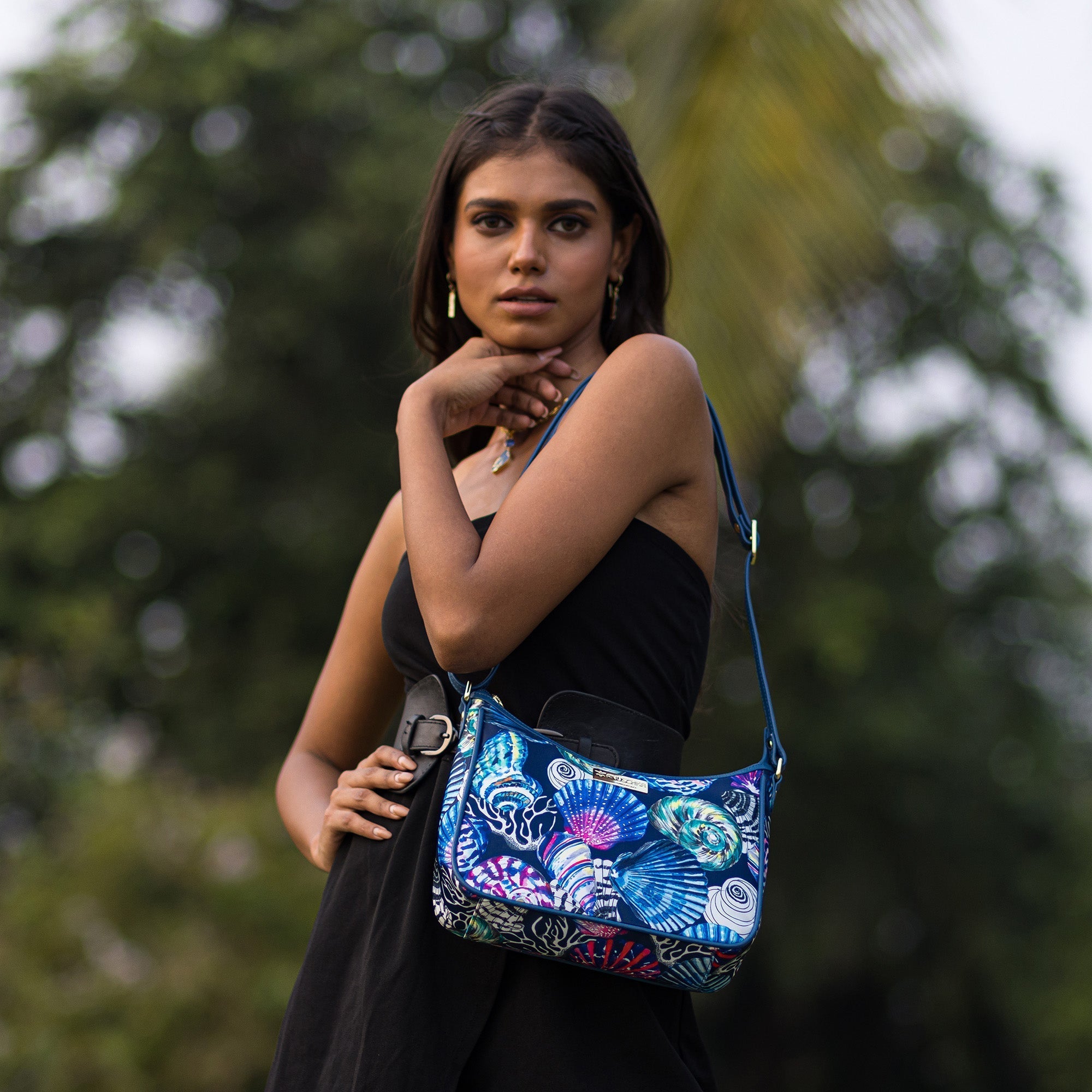 Woman posing outdoors with an Anuschka Fabric with Leather Trim East/West Hobo - 12013 featuring an adjustable handle.