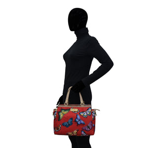 Mannequin dressed in black with a colorful butterfly-patterned Anuschka Fabric with Leather Trim Multi Compartment Satchel - 12014 featuring an adjustable strap.