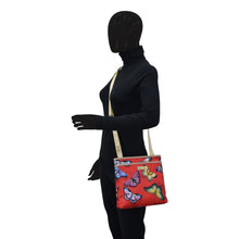 Load image into Gallery viewer, Mannequin wearing a black bodysuit and gloves, displaying an Anuschka Fabric with Leather Trim Crossbody with Slip Pocket - 12017 shoulder bag with adjustable handle.
