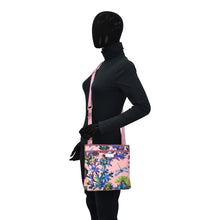Load image into Gallery viewer, A mannequin dressed in a black full-body outfit and a faceless head, wearing an Anuschka fabric with leather trim crossbody with slip pocket in pink with a tropical design and rear zippered pockets.
