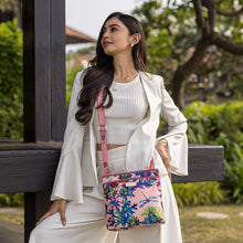 Load image into Gallery viewer, A woman in chic white attire posing with an Anuschka Fabric with Leather Trim Crossbody with Slip Pocket - 12017 bag that features an adjustable handle.
