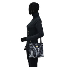 Load image into Gallery viewer, Mannequin displaying an Anuschka Fabric with Leather Trim Crossbody with Slip Pocket - 12017 shoulder bag with a tropical print design and rear zippered pockets.
