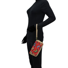 Load image into Gallery viewer, Person wearing a black turtleneck and black pants with a colorful patterned handbag over their shoulder, featuring an Anuschka Fabric with Leather Trim Wristlet Travel Wallet - 13000, which includes an RFID-protected zippered pocket.
