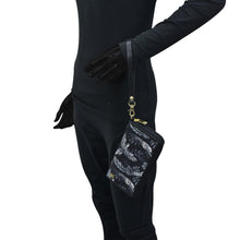 Load image into Gallery viewer, Person wearing a full black outfit with a black glove holding an Anuschka Fabric with Leather Trim Wristlet Travel Wallet - 13000, an RFID protected, patterned pouch with a zippered pocket.
