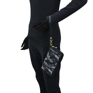 Person wearing a full black outfit with a black glove holding an Anuschka Fabric with Leather Trim Wristlet Travel Wallet - 13000, an RFID protected, patterned pouch with a zippered pocket.