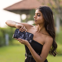 Load image into Gallery viewer, A woman in a strapless outfit checking the time on her Anuschka Fabric with Leather Trim Wristlet Travel Wallet - 13000 while holding a clutch with a zippered pocket.
