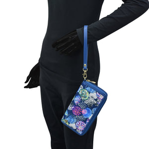 Person in a black bodysuit holding an Anuschka Fabric with Leather Trim Wristlet Travel Wallet - 13000 with a blue strap, featuring RFID protected card holders.