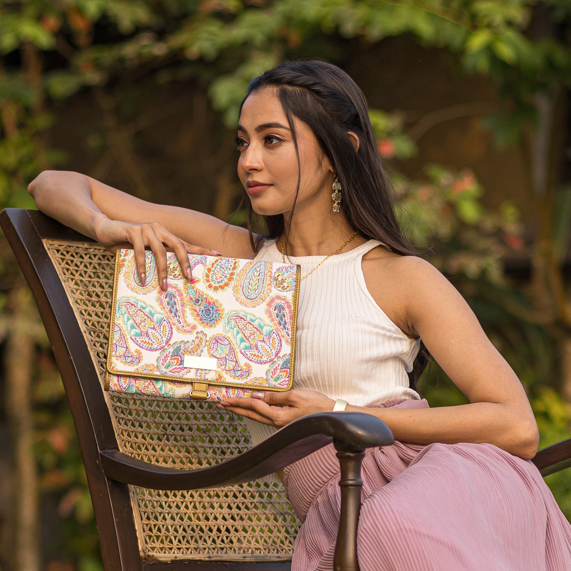 A woman posing with an Anuschka Fabric with Leather Trim Toiletry Case - 13001 featuring zippered pockets while sitting on a chair outdoors.