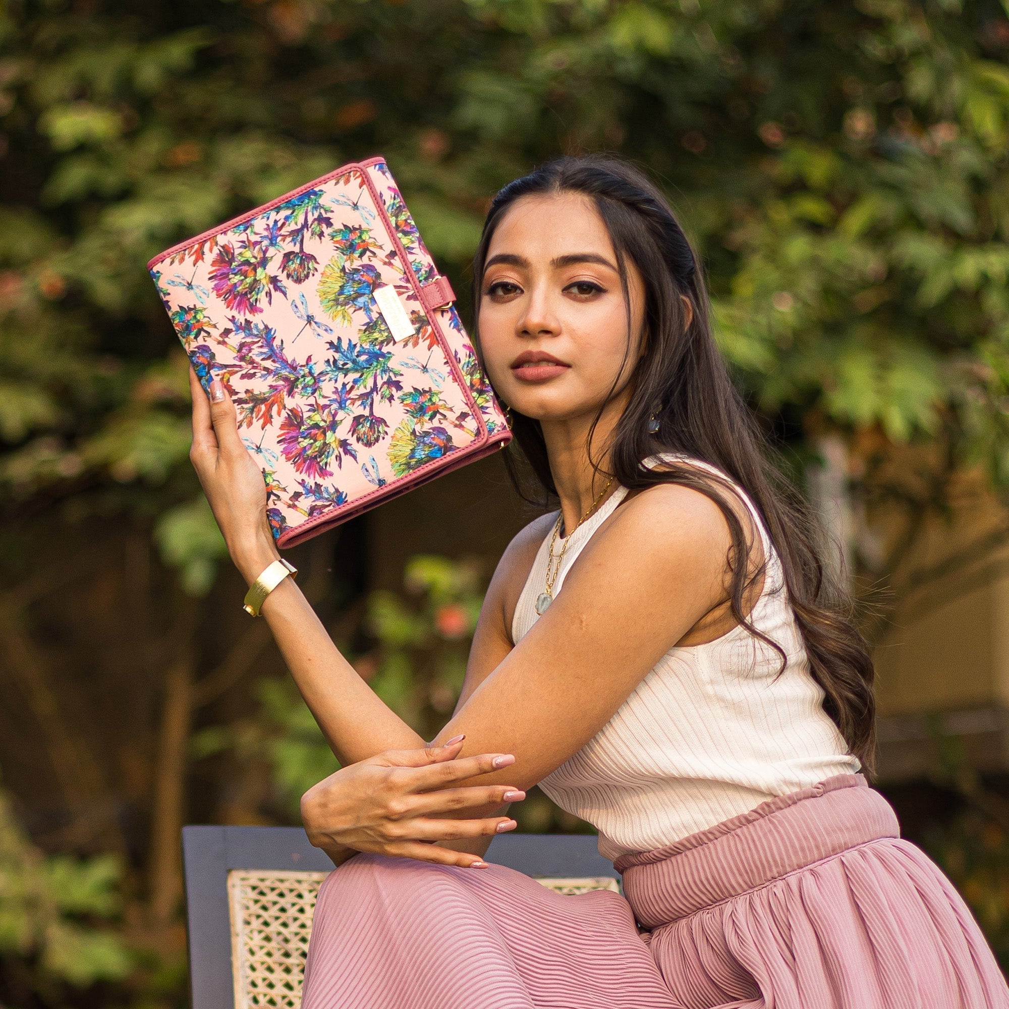 A woman holding an Anuschka Fabric with Leather Trim Toiletry Case - 13001 with snap button closure while sitting outdoors.