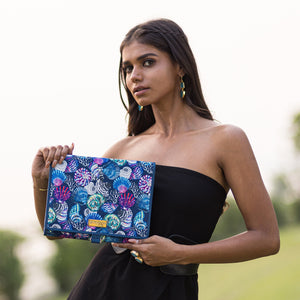 A woman holding a colorful Anuschka Fabric with Leather Trim Toiletry Case - 13001 with snap button closure outdoors.