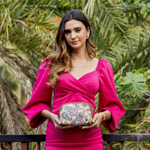 Woman in a pink dress holding an Anuschka Fabric with Leather Trim Dome Cosmetic Bag - 13002 clutch with a zip entry.