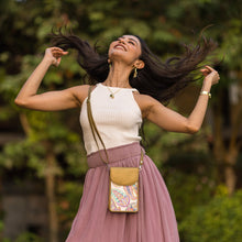 Load image into Gallery viewer, A joyful woman, her hair flowing freely with an Anuschka Fabric with Leather Trim Cell Phone Crossbody Wallet - 13005 slung over her shoulder, tosses her head back in a sunny outdoor setting.
