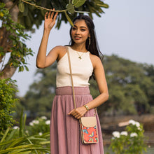 Load image into Gallery viewer, A woman in a white top and a pink skirt, holding a branch and wearing an Anuschka Fabric with Leather Trim Cell Phone Crossbody Wallet - 13005, poses outdoors with RFID protection.
