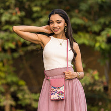 Load image into Gallery viewer, A woman smiling and posing with her hand on her head, wearing a white sleeveless top and pink skirt, accessorized with earrings, a necklace, and an Anuschka Fabric with Leather Trim Cell Phone Crossbody Wallet - 13005.
