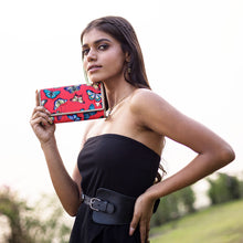 Load image into Gallery viewer, A woman in a black dress posing with a red floral, Anuschka RFID protected clutch.
