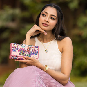 A woman holding an Anuschka Fabric with Leather Trim Three-Fold RFID Wallet - 13007 with zip pockets and card slots while posing thoughtfully.
