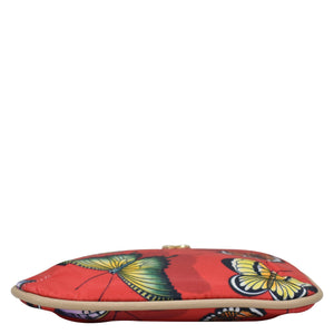 Colorful Anuschka clutch purse with butterfly pattern and key fobs against a white background.