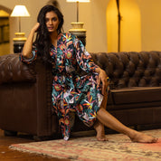 A woman in a floral dress and Anuschka silk robe posing on a leather couch in an elegant room.