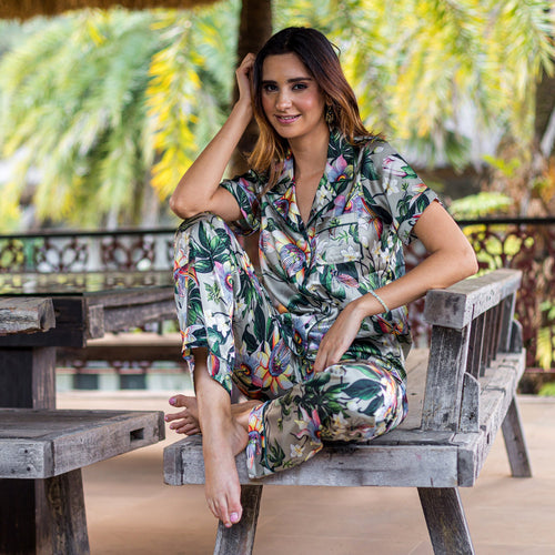 A woman in an Anuschka tropical print pajama set (3344) sitting casually on a wooden bench outdoors.