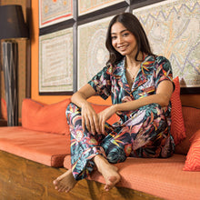Load image into Gallery viewer, Woman in a colorful Anuschka pajama set sitting on an orange couch with patterned pillows and artwork in the background.
