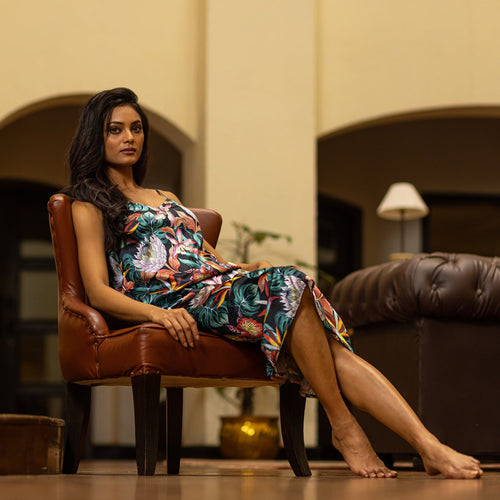 A woman in a chic floral Anuschka slip dress - 3346 sitting thoughtfully on a brown leather chair indoors.