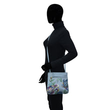 Load image into Gallery viewer, Silhouetted figure wearing a helmet and carrying an Anuschka Genuine Leather Slim Crossbody With Front Zip 452 with hand painted floral artwork.
