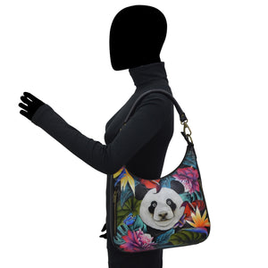 A person standing sideways with a black silhouette for a head, wearing a long-sleeve top and carrying an Anuschka Convertible Slim Hobo With Crossbody Strap - 662 with a panda design.