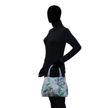 Load image into Gallery viewer, Mannequin in a black bodysuit holding an Anuschka Multi Compartment Satchel - 690 with an adjustable shoulder strap.

