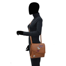 Load image into Gallery viewer, A person with an obscured face carrying an Anuschka Flap Messenger Crossbody - 692 handbag with butterfly designs and RFID protection stands against a white background.
