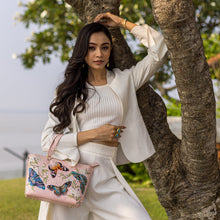 Load image into Gallery viewer, A woman in a white outfit poses with a pink, leather Anuschka Medium Tote - 693 near a tree.

