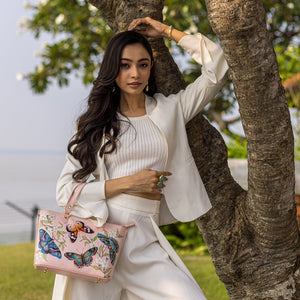 A woman in a white outfit poses with a pink, leather Anuschka Medium Tote - 693 near a tree.