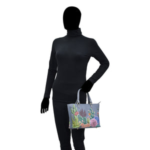 Mannequin in a black turtleneck and gloves holding a colorful floral, hand painted Anuschka Medium Tote - 693 with a zippered compartment.