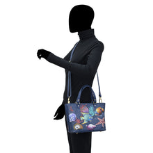 Load image into Gallery viewer, A silhouette of a person with a blacked-out face carrying a colorful, hand-painted marine life-themed Anuschka Medium Tote - 693.
