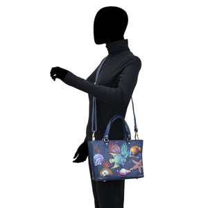 A silhouette of a person with a blacked-out face carrying a colorful, hand-painted marine life-themed Anuschka Medium Tote - 693.