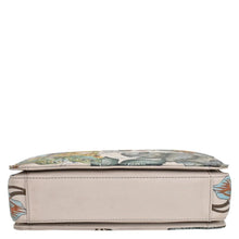Load image into Gallery viewer, A cushioned bench with a floral design, beige base, and Anuschka 696 triple compartment crossbody for organized traveling light.

