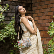 Load image into Gallery viewer, Woman traveling light and organized, posing with an Anuschka Triple Compartment Crossbody-696 against a brick wall with green foliage.
