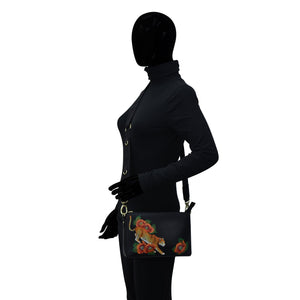Mannequin displaying a black Anuschka Triple Compartment Crossbody - 696 jacket and a purse with embroidered koi fish design.