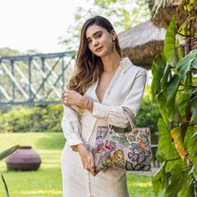 Load image into Gallery viewer, Woman posing with a chic, patterned Anuschka Medium Satchel - 697 in a garden setting.
