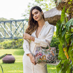 Woman posing with a chic, patterned Anuschka Medium Satchel - 697 in a garden setting.