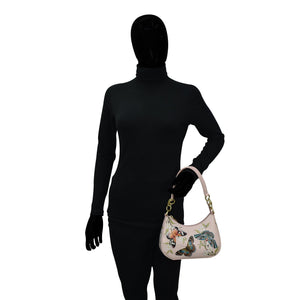 A mannequin dressed in a black bodysuit holding a Anuschka Small Convertible Hobo - 701 with floral and butterfly designs.