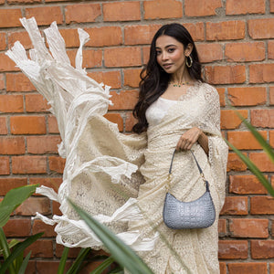 A woman in an elegant white dress holding an Anuschka Small Convertible Hobo - 701 poses against a brick wall.