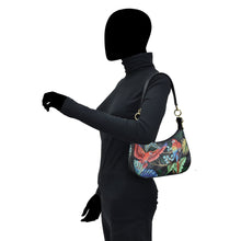 Load image into Gallery viewer, A person wearing a black outfit carrying a colorful Anuschka Small Convertible Hobo - 701 with a dinosaur print and a crossbody strap.
