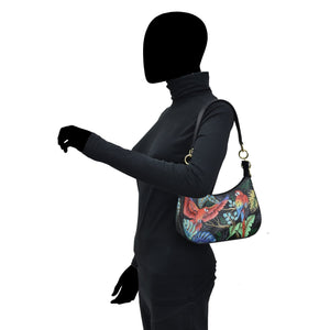 A person wearing a black outfit carrying a colorful Anuschka Small Convertible Hobo - 701 with a dinosaur print and a crossbody strap.