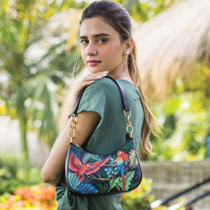 Woman posing with an Anuschka Small Convertible Hobo - 701 featuring a crossbody strap in a garden setting.