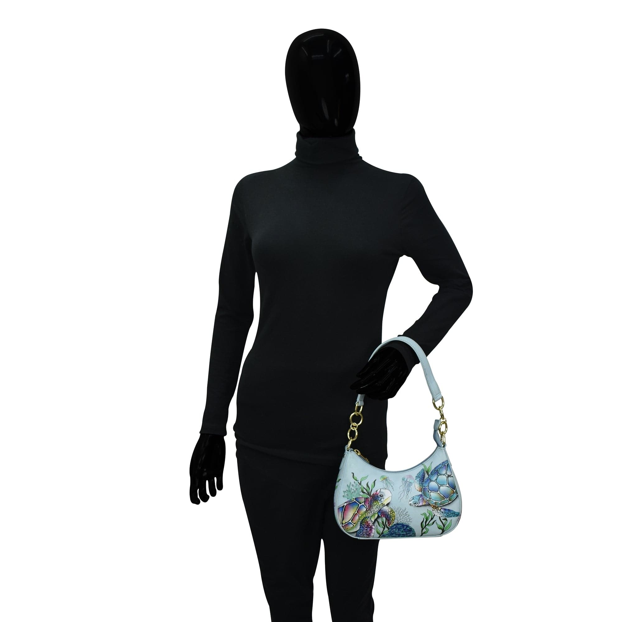Mannequin wearing a black full-body suit and gloves, holding an Anuschka Small Convertible Hobo - 701 with a floral and butterfly design.