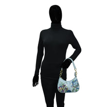 Load image into Gallery viewer, Mannequin wearing a black full-body suit and gloves, holding an Anuschka Small Convertible Hobo - 701 with a floral and butterfly design.
